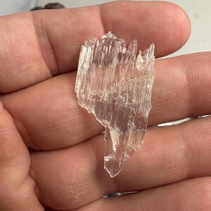 May include: A clear, colorless, jagged mineral specimen with a striated, crystalline texture. The piece features multiple sharp, vertical points and a translucent, glass-like appearance, showcasing natural geometric formations and irregular edges.