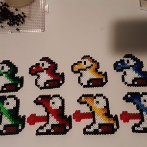 May include: Eight pixel art figures of Yoshi, a dinosaur-like character from the Super Mario video game series. The figures are made of colorful beads and are arranged in two rows of four. Each figure is a different color: green, red, yellow, blue, light green, dark red, light yellow, and dark blue.
