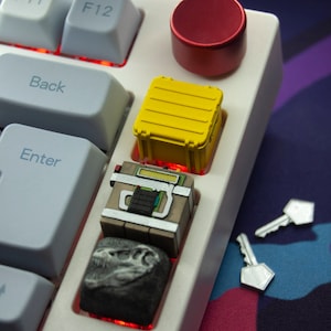 May include: A white mechanical keyboard with custom keycaps. The keycaps are themed around a military crate, a dinosaur, and a key. The keyboard is on a purple and blue background.