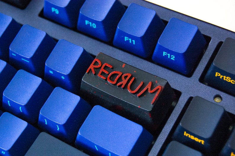 May include: A black keyboard with blue keys and a single red key with the word "REDЯUM" printed on it in red.