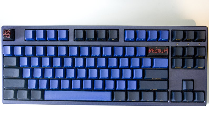 May include: A black and blue mechanical keyboard with blue keycaps and a black keycap with the word "REDRUM" written in red.