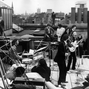 Peut inclure: Une photo en noir et blanc d'un groupe de musique se produisant sur un toit. Les membres du groupe jouent de la guitare et de la batterie. La photo est prise d'un angle bas, regardant le groupe.