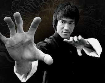 May include: A black and white photo of a man in a martial arts pose. He is wearing a black martial arts uniform with a white collar. His right hand is extended forward, palm facing the viewer. The background is a dark, textured surface with a stylized dragon design.