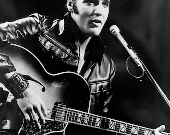 May include: A monochrome image of a man performing with an electric guitar and microphone. He is wearing a black leather jacket. The guitar is a hollow-body type. The image is set against a dark background.