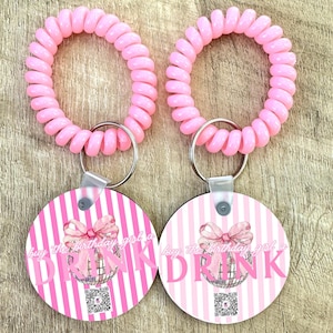 May include: Two pink spiral keychains with round, white and pink striped tags that say "buy the birthday girl a drink" with a pink bow and a disco ball graphic.