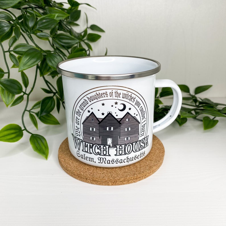 May include: White enamel mug with a black and gray graphic of a house with the text "We are the grand daughters of the witches you couldn't burn" and "Witch House Salem, Massachusetts".