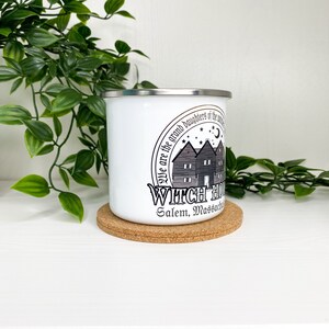 May include: White enamel camping mug with a black and gray graphic of a house with the text "We are the grand daughters of the witches" and "Witch House Salem, Massachusetts".