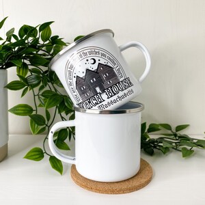 May include: Two white enamel mugs with a black and white graphic of a house with the text "These are the grand dames of the witches you couldn't burn Witch House Massachusetts".