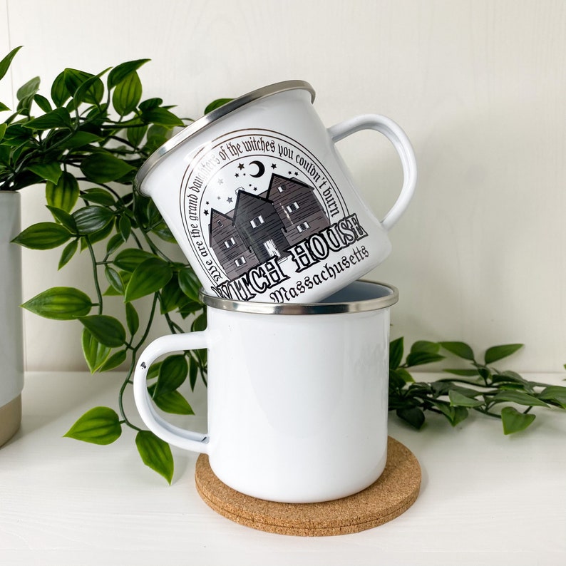 May include: Two white enamel mugs with a black and white graphic of a house with the text "These are the grand dames of the witches you couldn't burn Witch House Massachusetts".