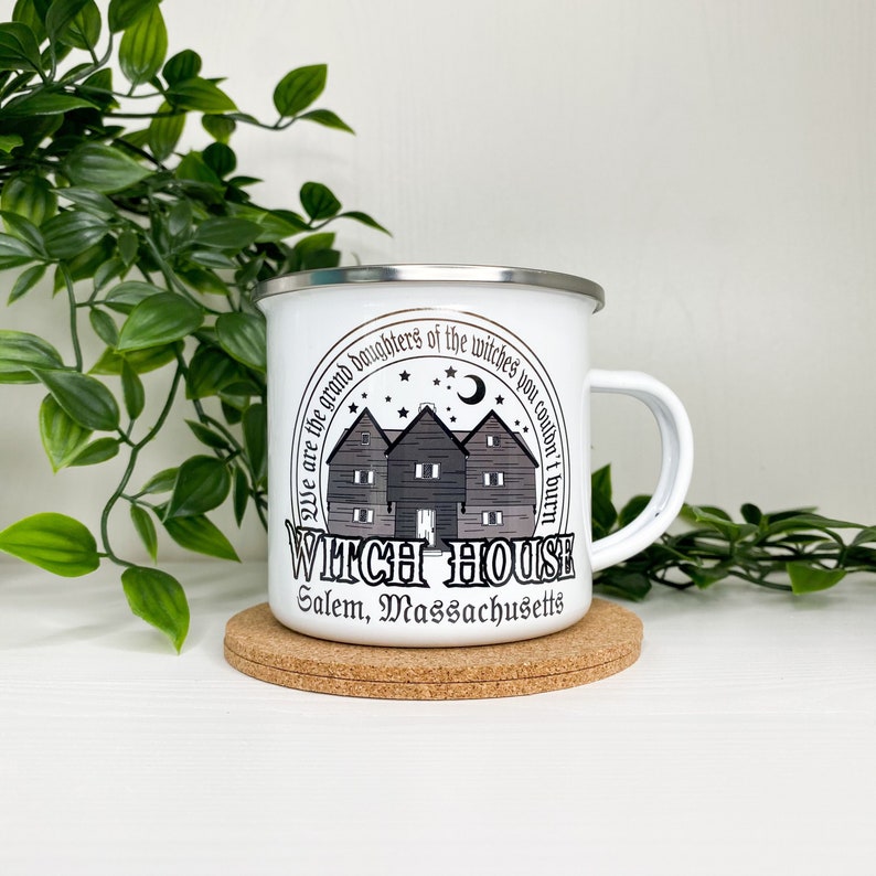 May include: White enamel camping mug with a black and white graphic of a house with the text "We are the grand daughters of the witches you couldn't burn Witch House Salem, Massachusetts".