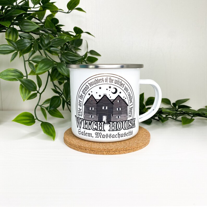 May include: White enamel mug with a black and white graphic of a house with the text "We are the grand daughters of the witches you couldn't burn. Witch House Salem, Massachusetts."