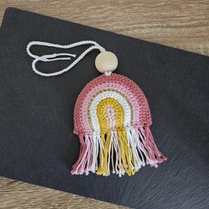 Peut inclure: Ornement arc-en-ciel crocheté à la main, avec des sections roses, jaunes et blanches, rehaussé d'un fil doré. Il comprend une perle en bois et un cordon blanc pour suspendre. Le bas est orné de franges assorties.