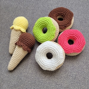 May include: Five crocheted food items, including two ice cream cones, a green donut, a white donut, and a pink donut.