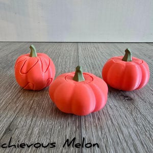 Könnte beinhalten: Drei leuchtend orangefarbene,  kürbisförmige Puzzle-Spielzeuge mit grünen Stielen. Die Kürbisse sind aus glattem Kunststoff.