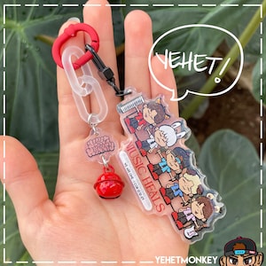 May include: A clear acrylic keychain with a red bell charm and a colorful illustration of a group of cartoon characters. The keychain features the text "MUSIC HEALS" and "WE ARE ONE 1 COR 12:12-27".