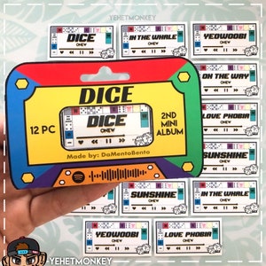 Puede incluir: Un conjunto de 12 pegatinas con un diseño de cinta de cassette con la palabra "DICE" y el artista "ONEW". Las pegatinas tienen un diseño colorido con un código de barras de Spotify y títulos de canciones. El embalaje dice "2ND MINI ALBUM".