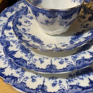 May include: A set of three blue and white porcelain plates with a gold trim. The plates feature a delicate floral pattern and are stacked on top of each other. A matching teacup sits on top of the plates.