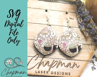 May include: A pair of Halloween-themed earrings with a white background and colorful details. The earrings feature a cauldron, ghosts, candy, and the word "BOO!" on each earring.