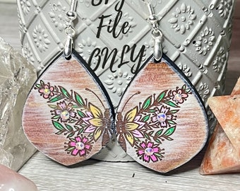 May include: A pair of wooden earrings featuring a butterfly and floral design. The butterfly is yellow, pink, and green, and the flowers are pink and green. The earrings are painted on a light brown background.