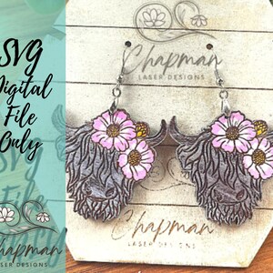 May include: A pair of wooden earrings featuring a Highland cow head with pink flowers. The earrings are on a white background with the text "Chapman Laser Designs".