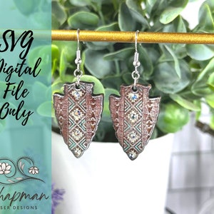 Op de afbeelding: Een paar zilveren pijlpunt oorbellen met een bruin, wit en turquoise patroon. De oorbellen hebben strass steentjes en hangen aan een gouden staaf.