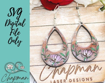 May include: A pair of wooden earrings with a teardrop shape and a floral design. The earrings are painted in shades of brown, pink, and green. The earrings are hanging from silver hooks.