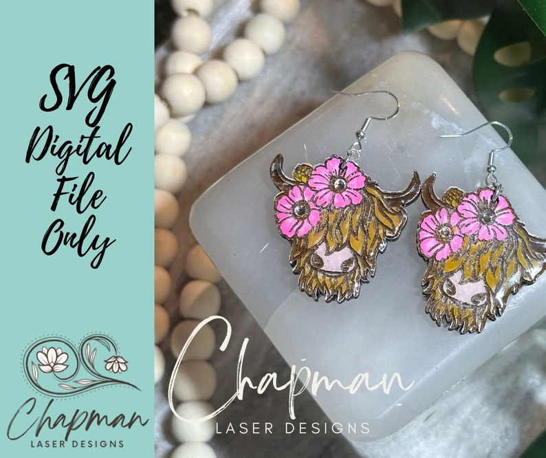 May include: A pair of earrings featuring a Highland cow design with pink flowers. The earrings are made of metal and have a silver finish.