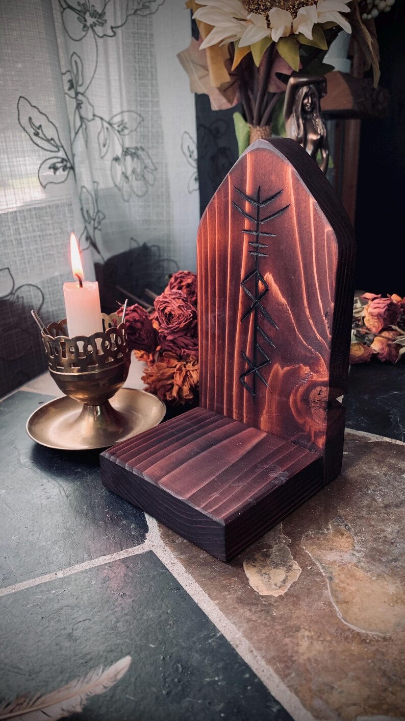 K&ouml;nnte beinhalten: Ein dunkelbrauner Holzaltar mit einem geschnitzten Runensymbol. Der Altar hat eine Ablagefl&auml;che zum Aufstellen von Kerzen oder anderen Gegenst&auml;nden. Der Altar steht auf einem gefliesten Boden.