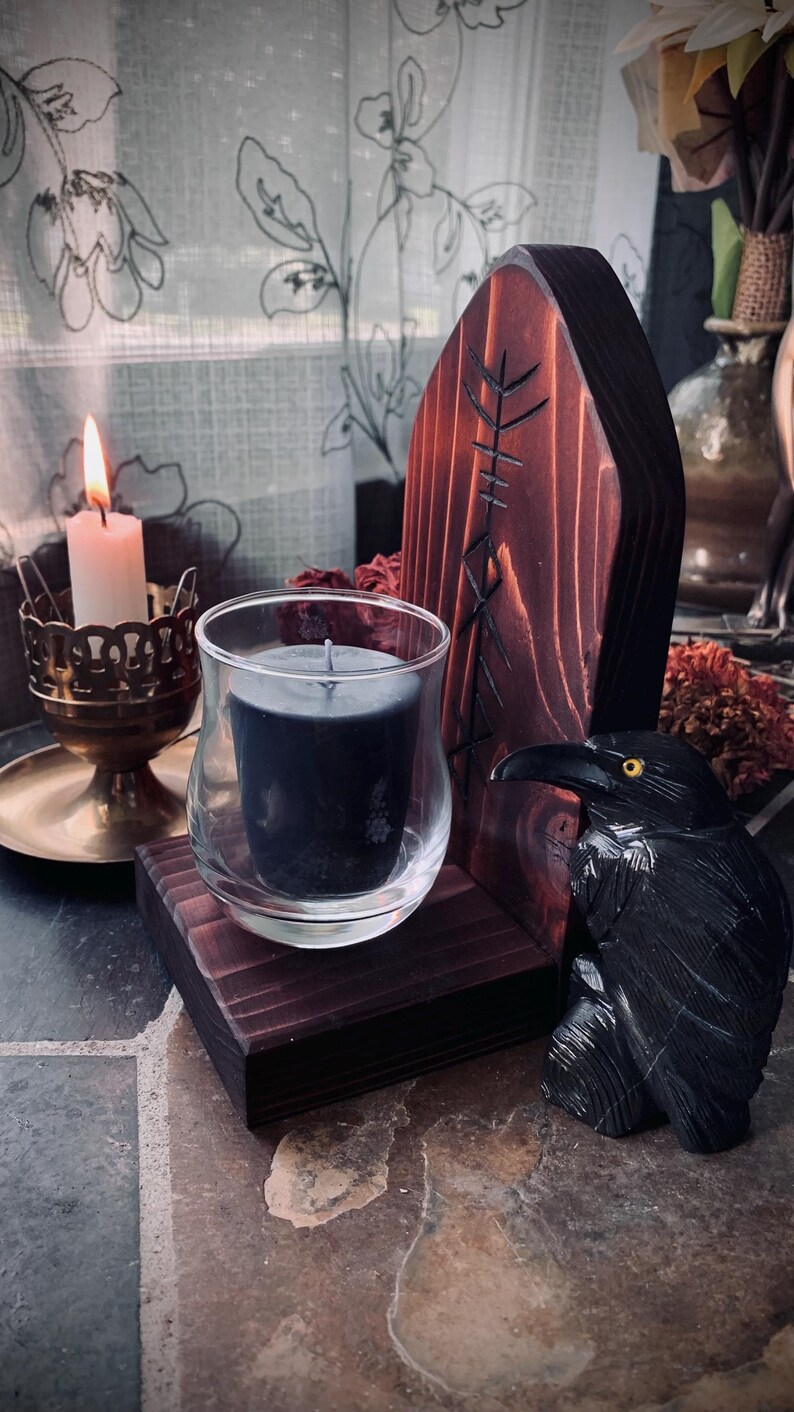 K&ouml;nnte beinhalten: Ein Kerzenhalter aus Holz mit einem geschnitzten Raben und einer schwarzen Kerze. Der Halter hat eine dunkle Holzoptik und ist mit einem Runenzeichen verziert.