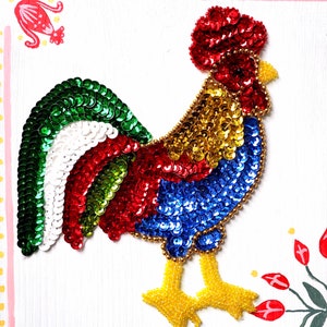 May include: A colourful rooster made of sequins, with a red head, green tail feathers, and yellow legs. The rooster is on a white background.