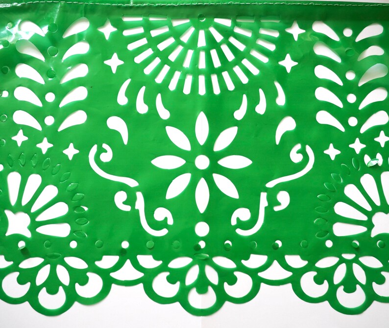 May include: Green paper banner with a traditional Mexican design featuring cut-out flowers, stars, and swirls. The banner is made of thin paper and has a delicate, intricate design.