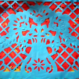 May include: A blue paper cutout of a traditional Mexican design with intricate floral patterns. The cutout is layered over a red and yellow paper background.