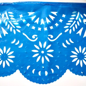 May include: Blue paper with white cut-out designs. The design features flowers, leaves, and geometric shapes. The paper has a scalloped edge.
