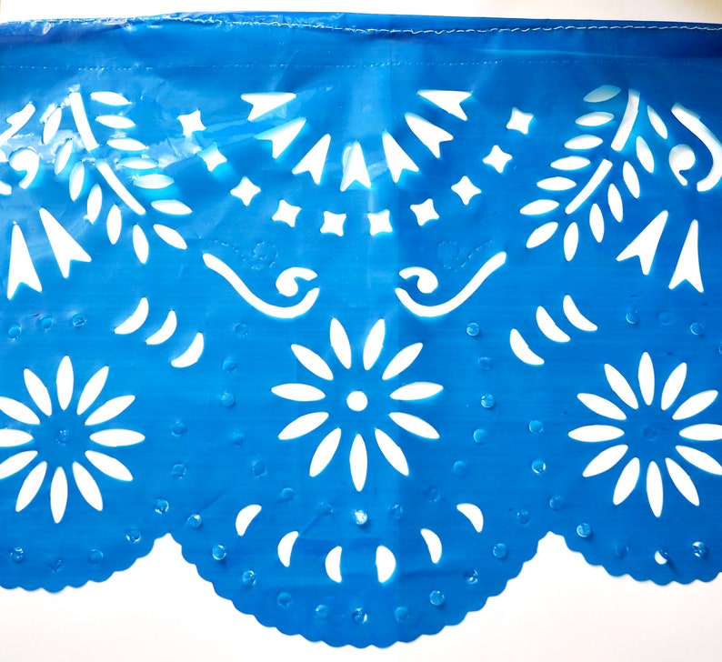 May include: Blue paper with white cut-out designs. The design features flowers, leaves, and geometric shapes. The paper has a scalloped edge.