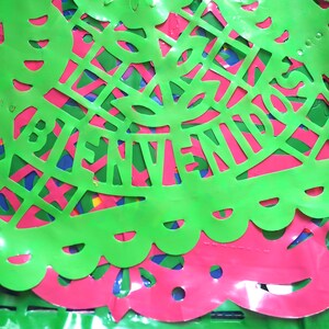 May include: Green and pink paper cutouts with the word "BIENVENIDOS" in the center. The cutouts are layered and have a shiny finish.