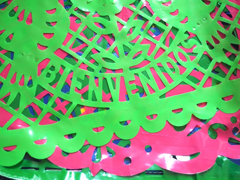 May include: Green and pink paper cutouts with the word "BIENVENIDOS" in the center. The cutouts are layered and have a shiny finish.