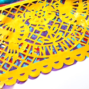 May include: A yellow paper cutout with a decorative design, featuring a bird and the word "Bienvenidos". The cutout is layered over a purple, blue, and red paper background.