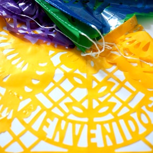 May include: A yellow paper banner with a cut-out design featuring the words "Bienvenidos" in Spanish. The banner is part of a string of colorful paper banners.