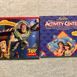 May include: Two vintage CD-ROM computer game boxes. One is "Toy Story Animated Storybook" featuring Buzz Lightyear and Woody. The other is "Disney's Aladdin Activity Center" with Aladdin, Jasmine, and the Genie.