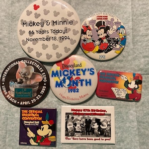 May include: A collection of vintage Disney pins and buttons. The pins feature Mickey and Minnie Mouse, Dumbo, and other Disney characters. Some pins commemorate events like Mickey's 66th anniversary and the Disneyland Hotel.