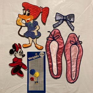 May include: Assortment of embroidered patches featuring cartoon characters and decorative elements. Includes a Woody Woodpecker patch, a Minnie Mouse patch, a blue bow, a pair of pink ballet slipper patches, and a card of balloon patches. The card reads "Wrights".