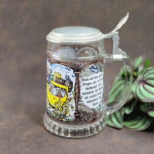 Peut inclure: Chope à bière en verre transparent avec couvercle et poignée articulés en métal. La chope présente une illustration colorée d'une voiture jaune et du texte en allemand. La chope est décorée d'un couvercle et d'une poignée en métal argenté.