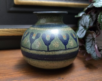 Könnte beinhalten: Eine kleine, runde, grüne und blaue Keramikvase mit geometrischem Muster. Die Vase hat eine gesprenkelte Glasur und ein dunkelblaues Band um den oberen Rand.