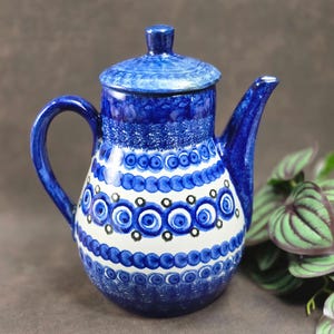 May include: A blue and white ceramic coffee pot with a lid. The pot features a handle and spout, and is decorated with a pattern of blue circles and white stripes. The pot is a decorative item.