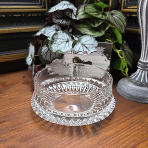Könnte beinhalten: Eine klare Glasschüssel mit einem dekorativen, geschliffenen Glasdesign. Die Schüssel hat einen breiten, flachen Boden und einen leicht ausgestellten Rand.