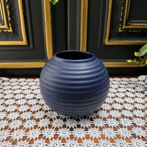 Könnte beinhalten: Eine dunkelblaue Keramikvase mit gerippter Textur. Die Vase ist rund und hat eine breite Öffnung.