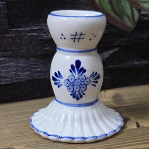 Könnte beinhalten: Weißer Kerzenhalter aus Keramik mit blau-weißem Blumendesign. Der Halter hat einen geriffelten Sockel und eine breite Öffnung oben.