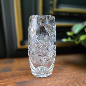 Könnte beinhalten: Eine klare Glasvase mit geschnittenem Kristallmuster. Die Vase hat eine zylindrische Form und ist etwa 15 cm hoch.