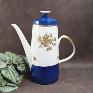 Könnte beinhalten: Eine weiß-blaue Porzellan-Kaffeekanne mit goldenem Griff und Blumendesign. Die Kanne hat einen blauen Deckel und Boden, mit einem weißen Mittelteil, der mit goldenen Rosen verziert ist. Der Ausguss ist lang und schlank.