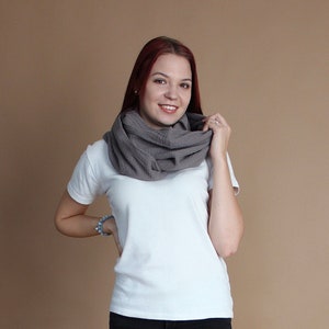 May include: A woman wearing a white t-shirt and black jeans with a gray infinity scarf around her neck.